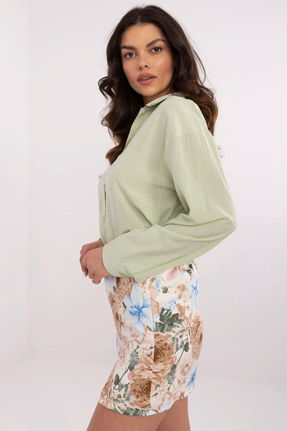 Side view of NM's elegant long sleeve women's shirt in green, showcasing its fitted silhouette and classic collar, complemented by a chic floral skirt.