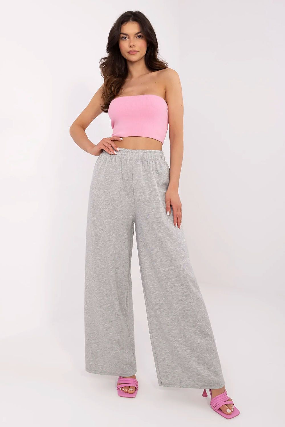 Elegantly styled woman in a pink strapless top paired with high-waist wide leg trousers in grey, showcasing Italy Moda's blend of comfort and luxury.