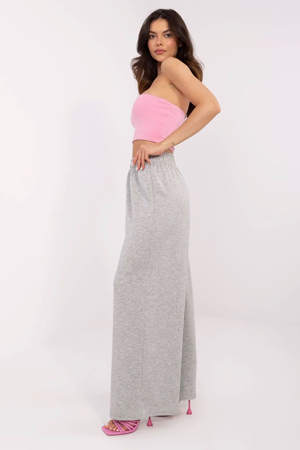 Side view of a fashionable woman in a pink strapless top with high-waist grey wide leg trousers, embodying Italy Moda's modern and comfortable aesthetic.