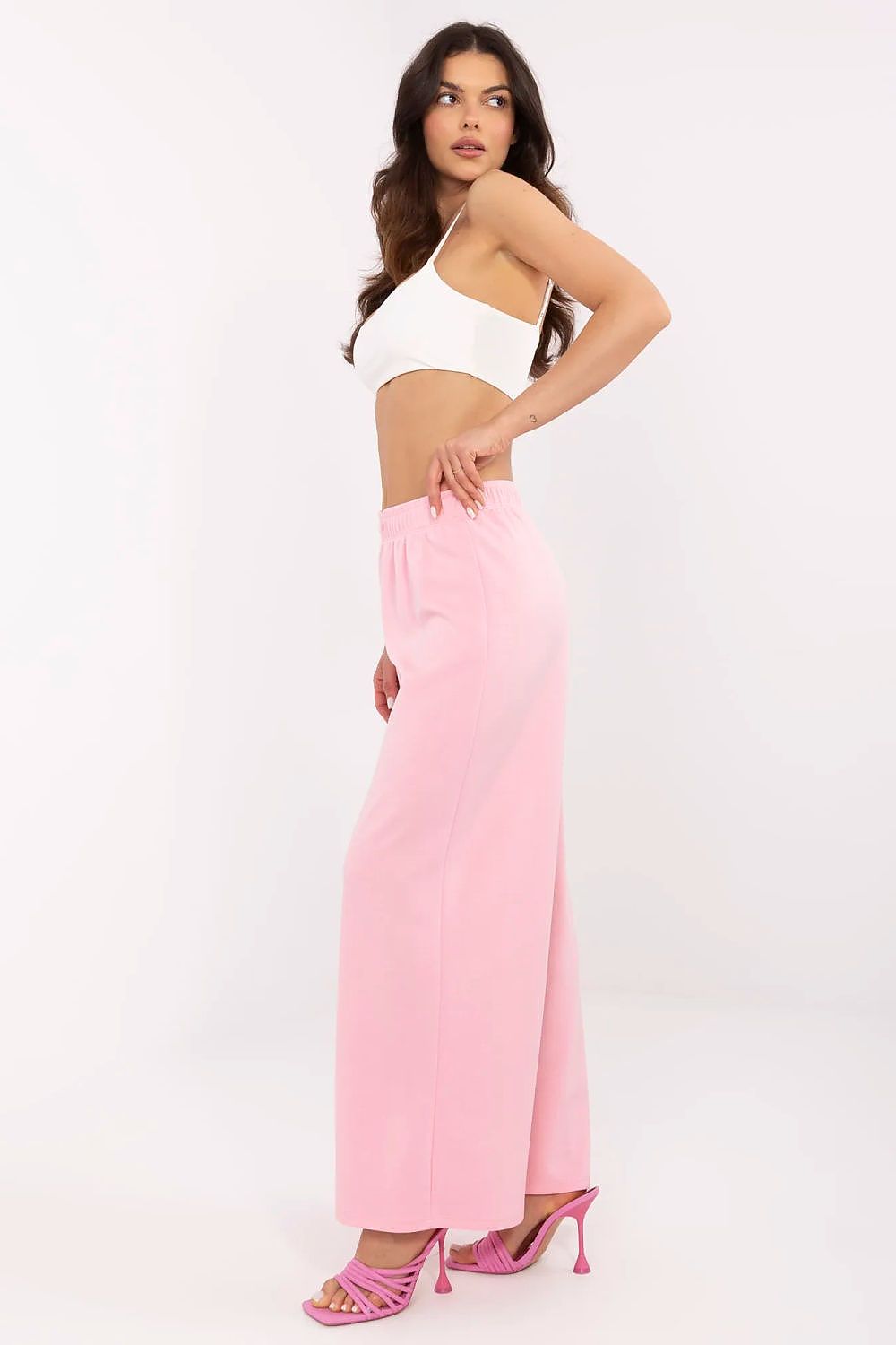 Side view of an elegant woman in a white crop top and pink high-waist wide leg trousers, epitomising the luxurious comfort offered by Italy Moda.