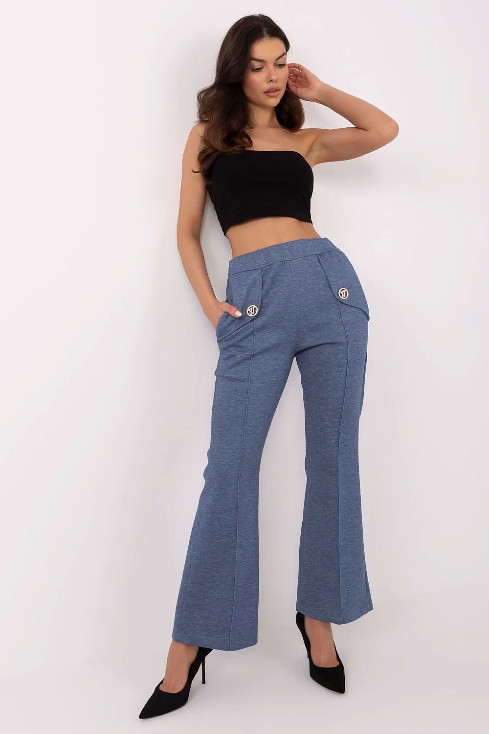 Elegant woman wearing Italy Moda high waist bell-shaped sweatpants in blue, styled with a black crop top and pointed heels, showcasing side pockets and a chic silhouette.