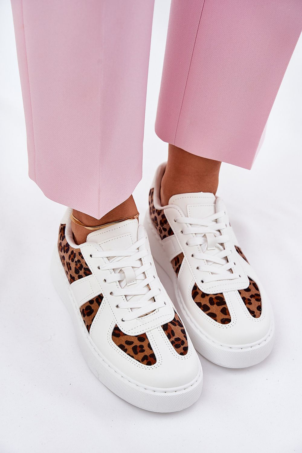 Close-up of stylish white and leopard print women's sneakers by Step in style, elegantly complemented by pink trousers for a fashionable outfit.