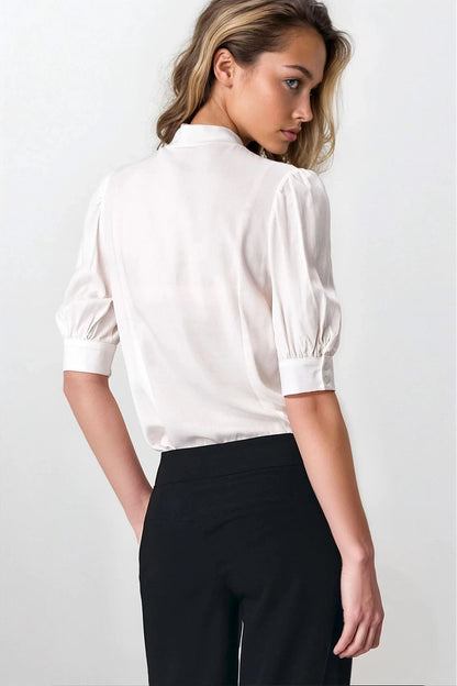 Chic Nife blouse in a luxurious setting, designed with a neck tie and graceful puffy sleeves, ideal for those seeking a blend of elegance and comfort.
