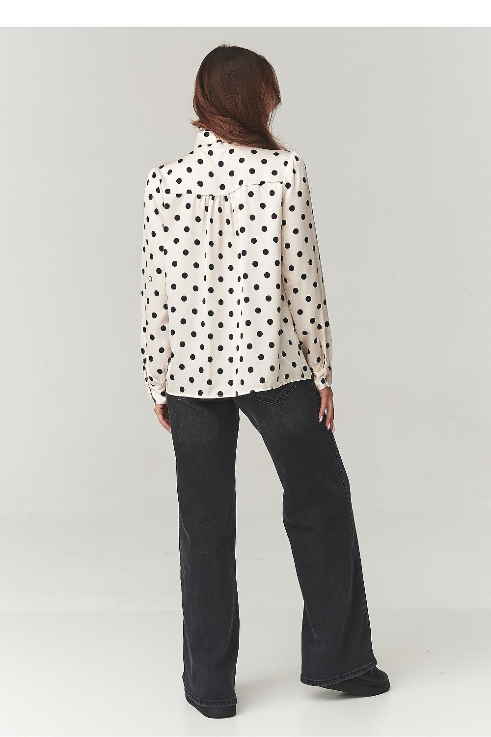 Model wearing Makadamia's classic polka dot shirt with bow, displaying the delicate fabric and flattering fit ideal for chic office wear or social events.