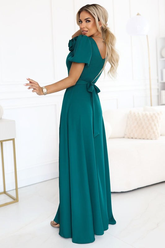 Chic bottle green evening gown by Numoco with a delicate slit and removable shoulder rose, ideal for weddings and special events.