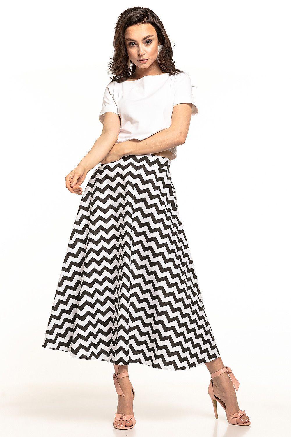 Elegant 1950s-inspired midi skirt by Tessita, featuring a striking black and white chevron design, beautifully styled on a model wearing a white top and pink heels.