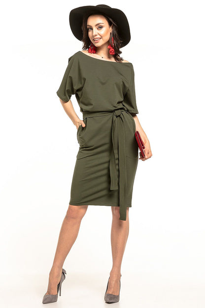 Elegant lady in a luxurious olive green midi dress with kimono sleeves and a belt by Tessita, styled with a black hat and red accessories.