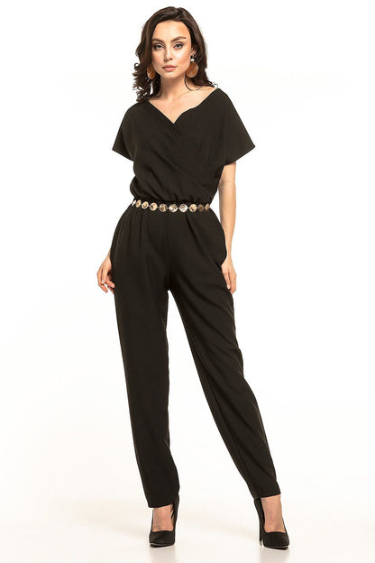 Chic Tessita jumpsuit in classic black adorned with short sleeves and an elegant envelope neckline. Model presents a fashionable silhouette with a gold belt.