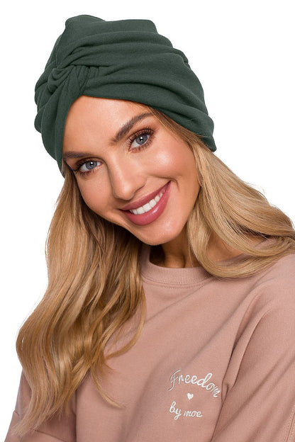 Elegant woman wearing a luxury lightweight knitted cap with a turban pattern in deep green, highlighting comfort and style by Moe.