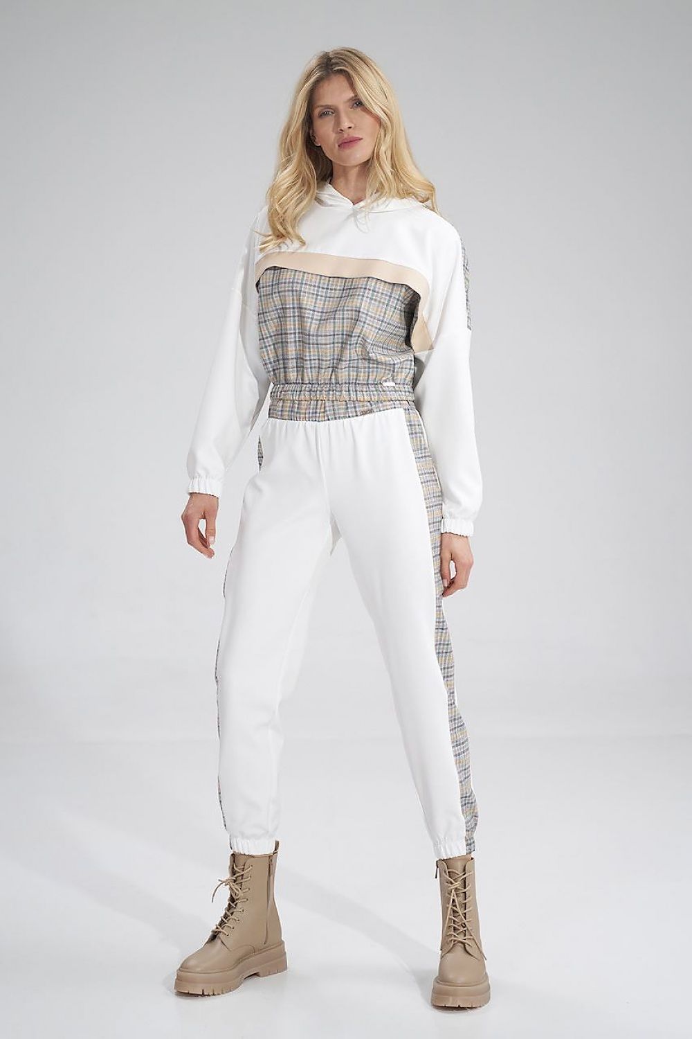 Stylish woman modelling Figl tracksuit trousers with contrasting plaid design, elevated sporty look, featuring a wide elastic waistband and chic brown lace-up boots.