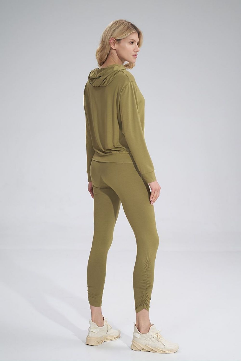 Model in Figl long leggings with creased detailing and wide waistband, seen from the back, paired with a stylish hooded top, exuding luxury and comfort.