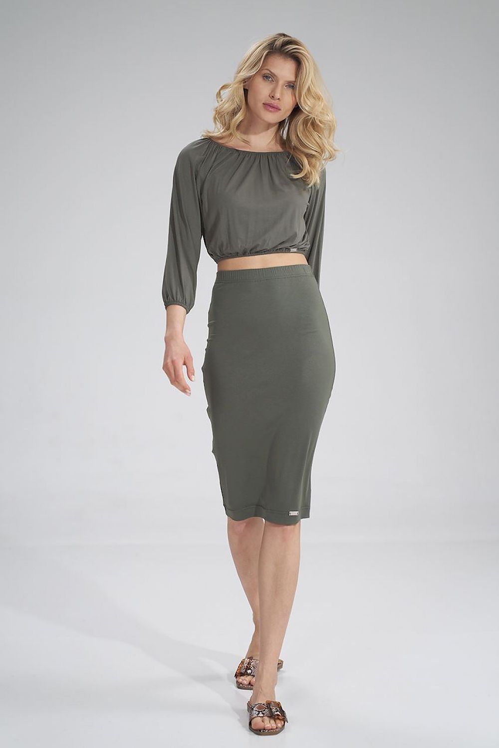 Sophisticated model in an olive Figl pleated blouse and skirt, spotlighting timeless elegance in a luxury fashion setting.