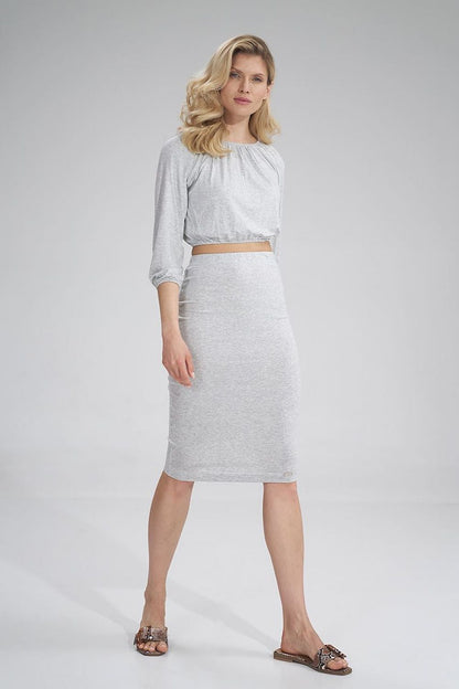 Front view of a blonde female model elegantly dressed in Figl's pleated blouse and grey fitted skirt, highlighting a chic and luxurious style.