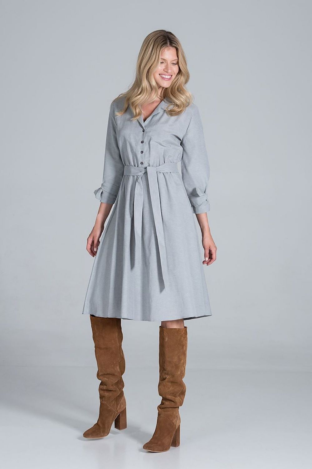 Elegant Midi Dress by Figl with Jacket-Style V-Neck, Flared Hem & Tie Belt, styled in a light grey fabric, displayed with a cheerful smile and knee-high brown boots, embodying sophistication and elegance.