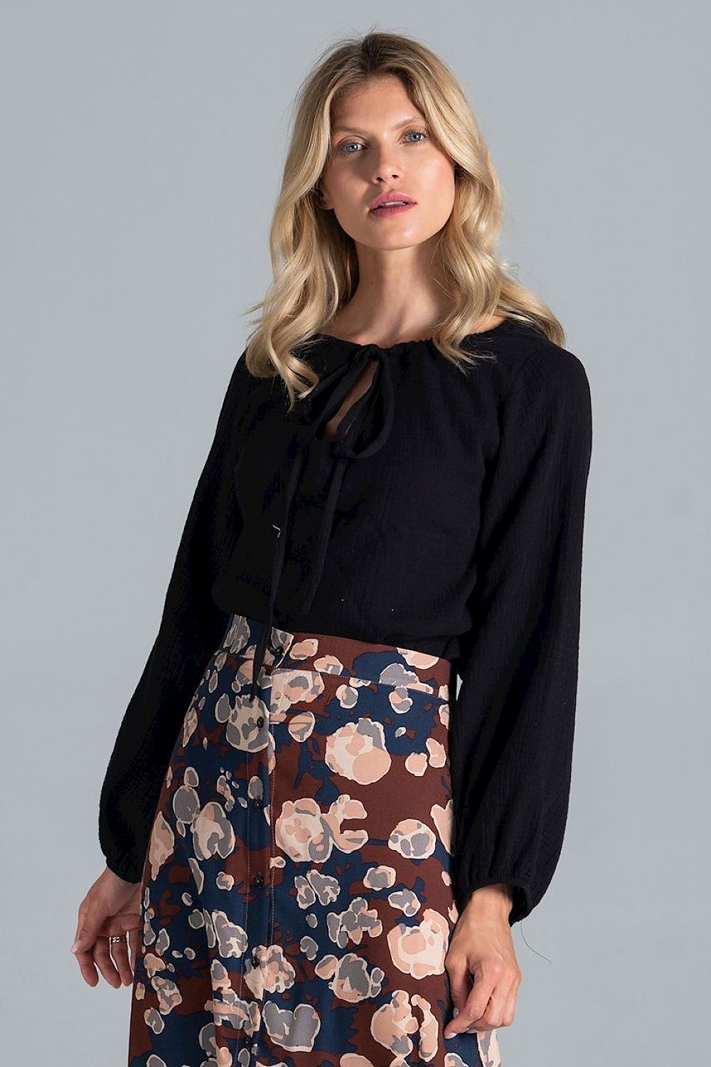 Close-up of the Luxury Figl Blouse in black, featuring a half-round neckline with tie detail and long sleeves, paired with a floral skirt.