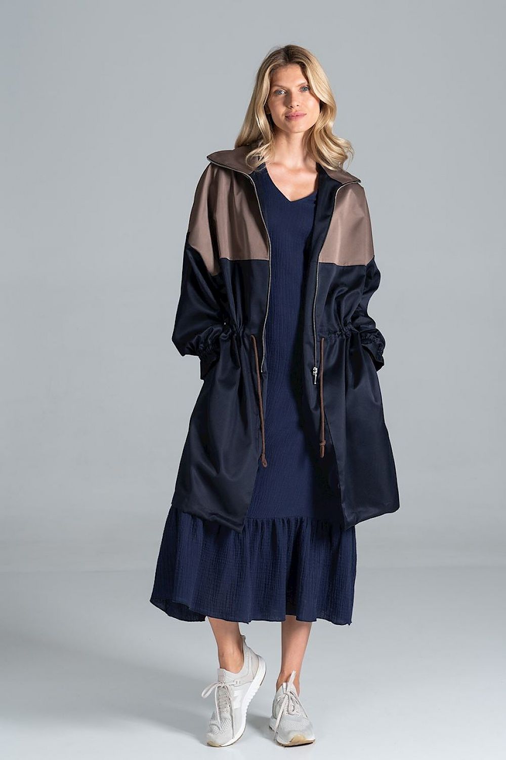 Elegant two-coloured autumn parka coat with drawstring waist and zip fastening by Figl, modelled by a woman wearing a navy dress and white sneakers, elegant styling.