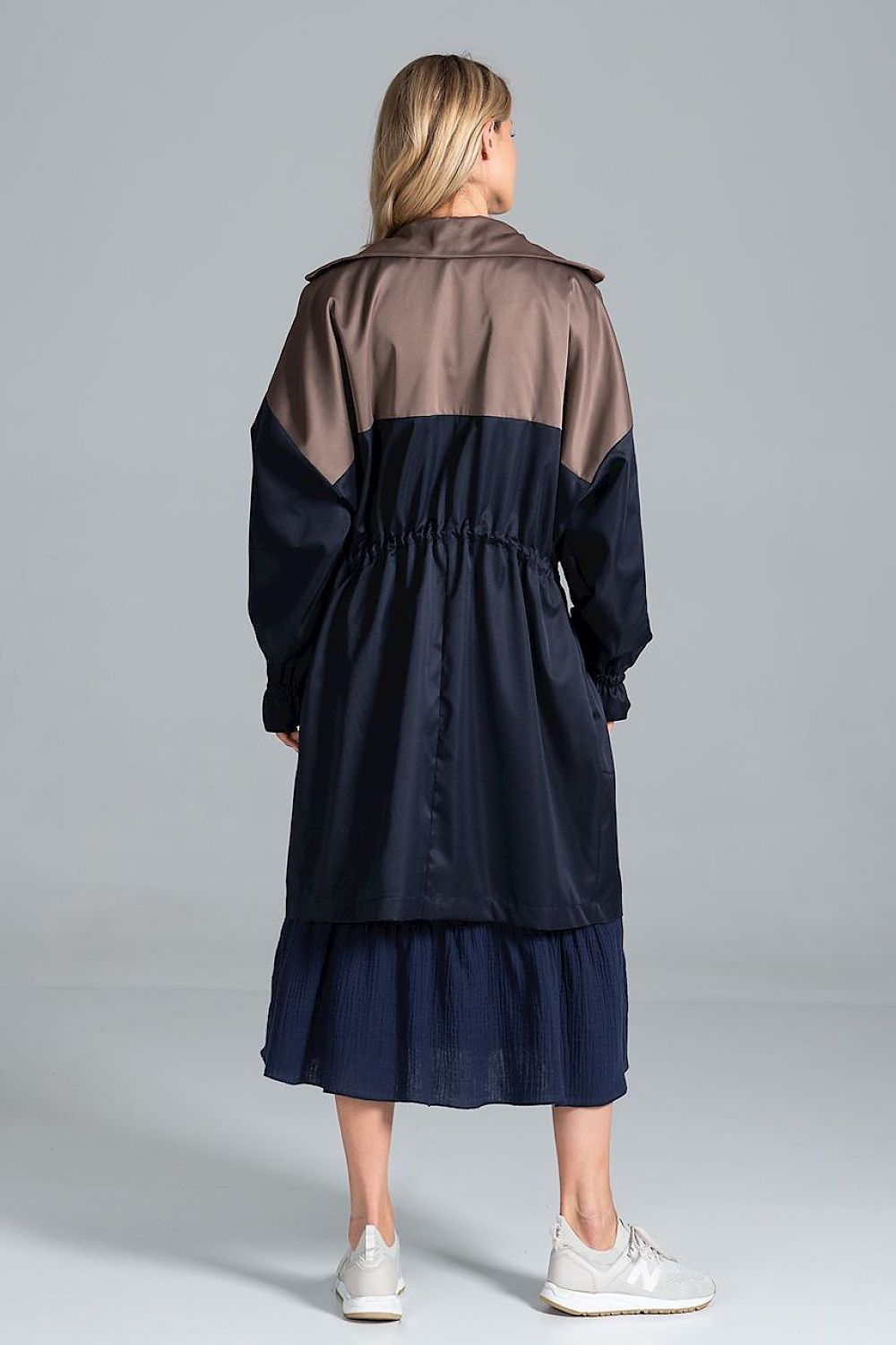 Back view of the elegant two-coloured autumn parka coat with drawstring waist and zip fastening by Figl, worn by a model in a navy dress with a tiered hem.
