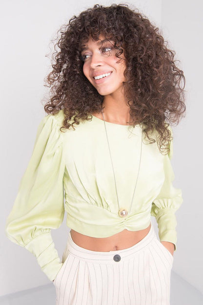 Elegant model showcasing a lime long sleeve viscose blouse with unique back neckline by Sally Fashion, paired with stylish light-coloured trousers, exuding a luxurious and fashionable vibe.
