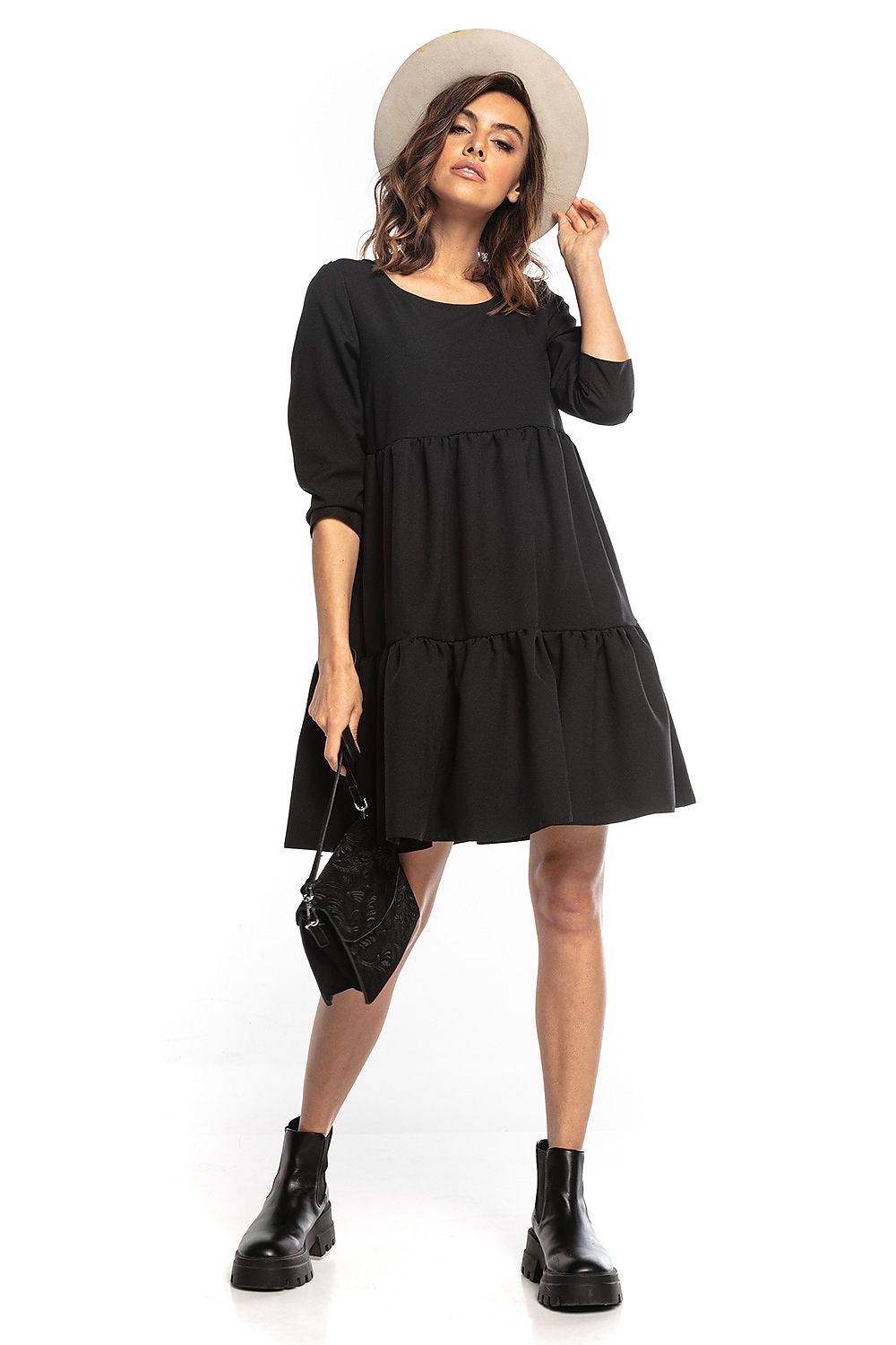Model showcasing an elegant black mini dress with ruffled flared cut, 3/4 sleeves, and a deep back neckline by Tessita, styled with a chic hat and trendy accessories.