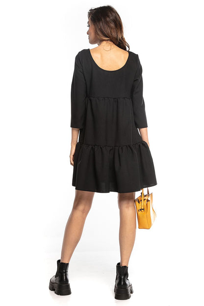 Back view of a model in a sophisticated black mini dress featuring ruffled flared design, 3/4 sleeves, and a deep neckline, presented by Tessita.