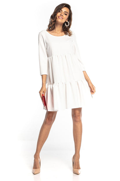 Model elegantly presenting a white mini dress with ruffled flared cut and 3/4 sleeves, complemented by stylish accessories, designed by Tessita.