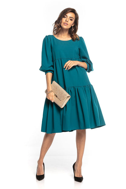 Tessita Elegant Bouffant Sleeve Day Dress in teal, featuring a ruffled flared cut and a chic boat neckline. The model is styled with a gold clutch and high heels, showcasing a sophisticated and luxurious ensemble.