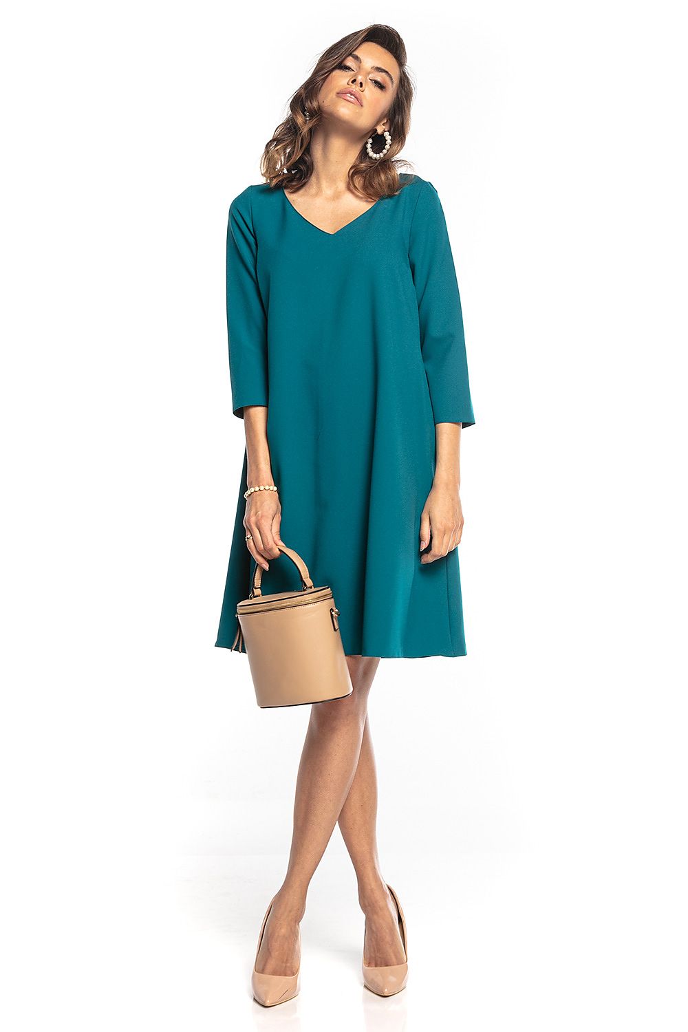 Elegant Tessita trapeze dress in teal, featuring 3/4 sleeves and a pointed neckline, styled with a chic handbag.