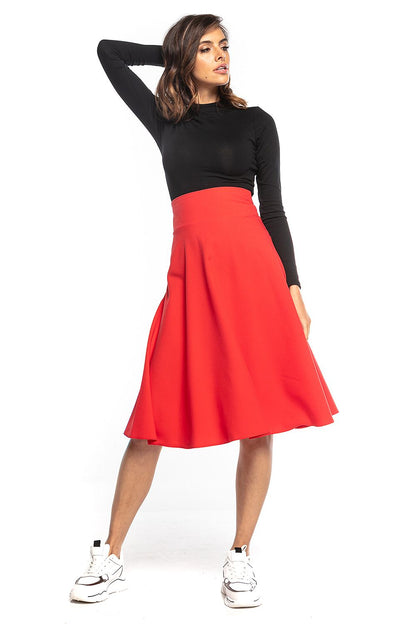 Elegantly styled model showcasing a vibrant red midi skirt with a high waist and decorative zipper, designed by Tessita, complemented with a black long-sleeve top and chic white sneakers.