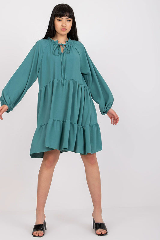 Elegant luxury flared dress with long sleeves and tie neckline, showcasing a model in a rich teal colour, perfect for sophisticated occasions.