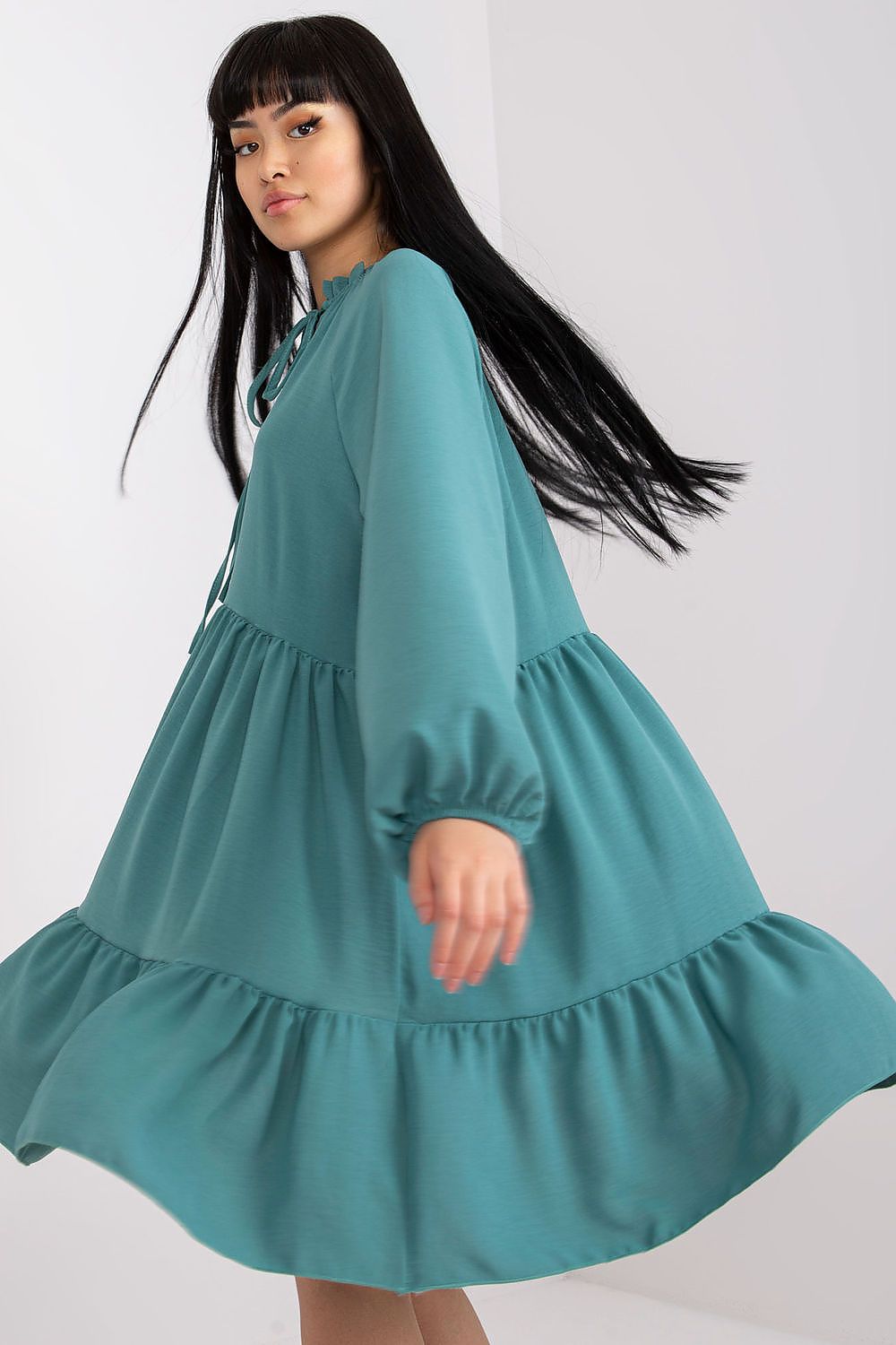 Model twirling in a stunning luxury flared dress with flowing tiers and long sleeves in teal, ideal for enhancing elegance at formal events.