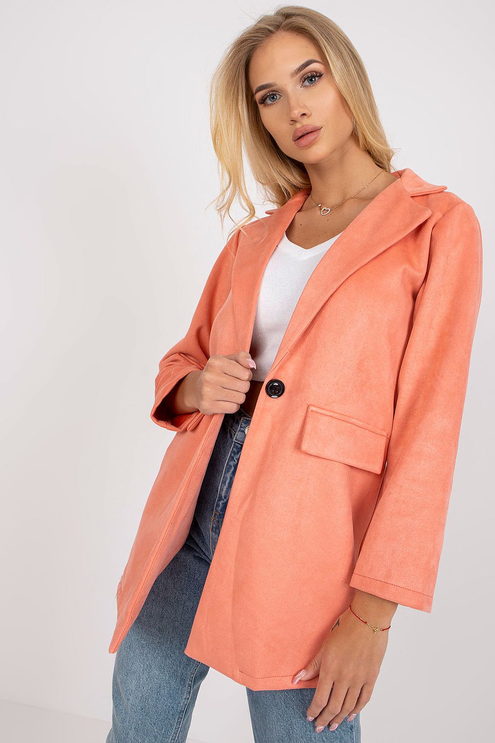 Elegant woman wearing a luxury imitation suede jacket in coral, featuring a sleek design with a zippered front, complemented by a casual white top and denim jeans.