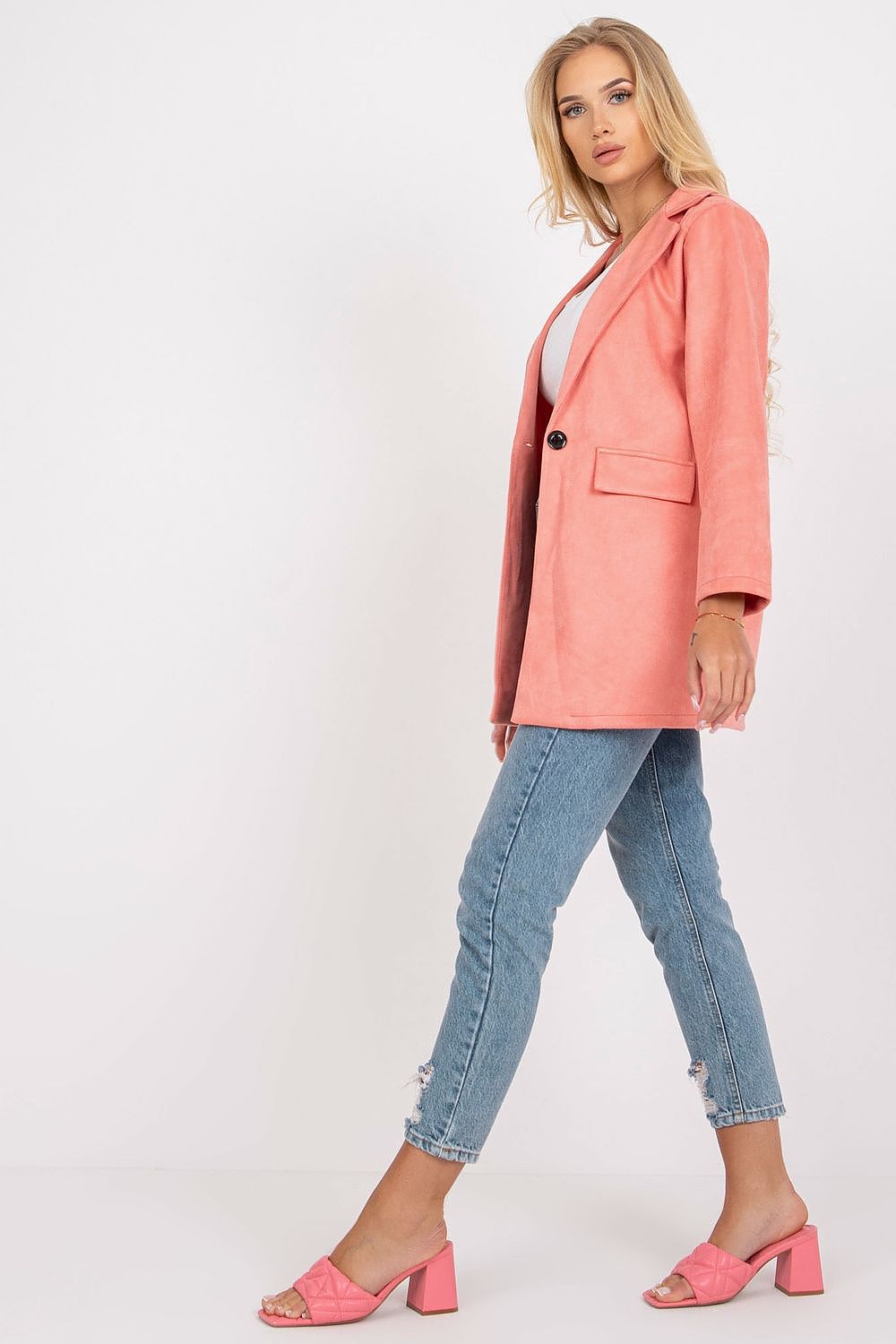 Sophisticated woman in a coral imitation suede jacket, depicted in a side view, paired with ripped jeans and pink block-heeled sandals, embodying modern elegance.