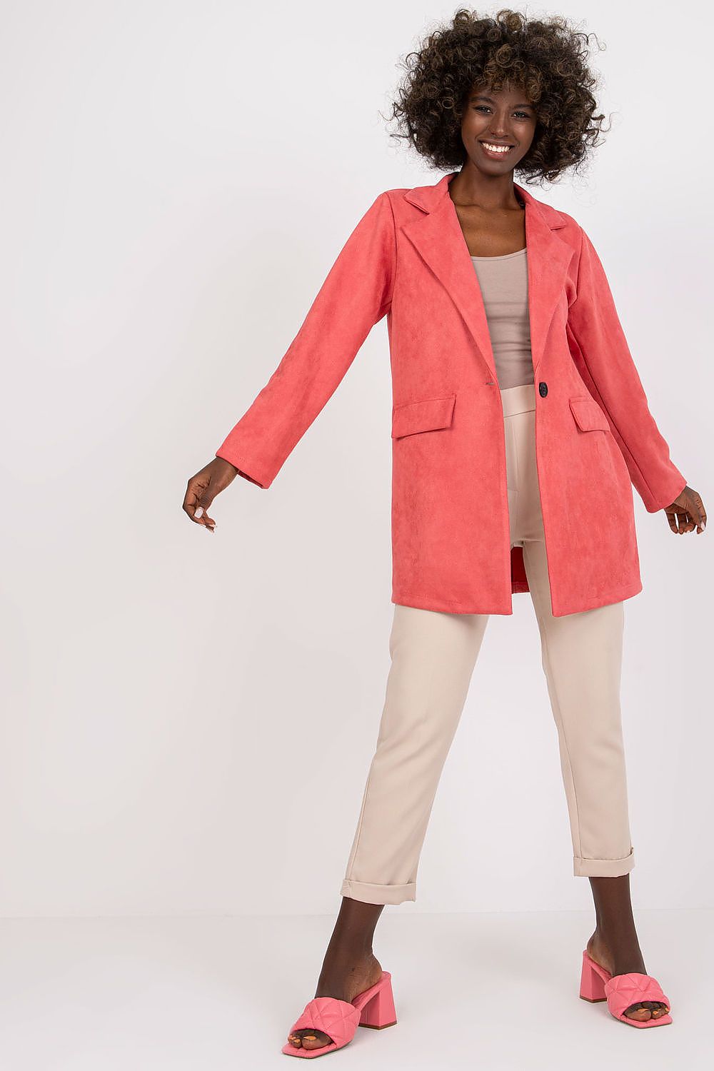 Stylish model wearing a luxury imitation suede jacket in coral, featuring a zippered design, paired with beige trousers and pink block-heeled sandals, showcasing elegance and versatility for any occasion.