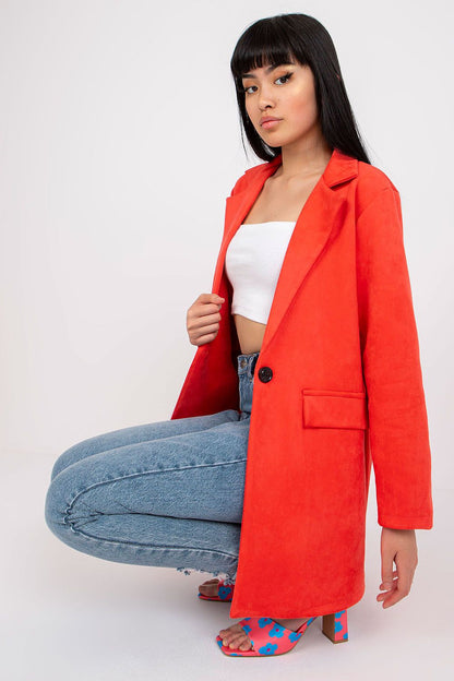 Fashionable model styled in a vibrant red imitation suede jacket, seated in trendy ripped jeans, complemented by blue floral high-heeled sandals, perfect for a chic and casual look.