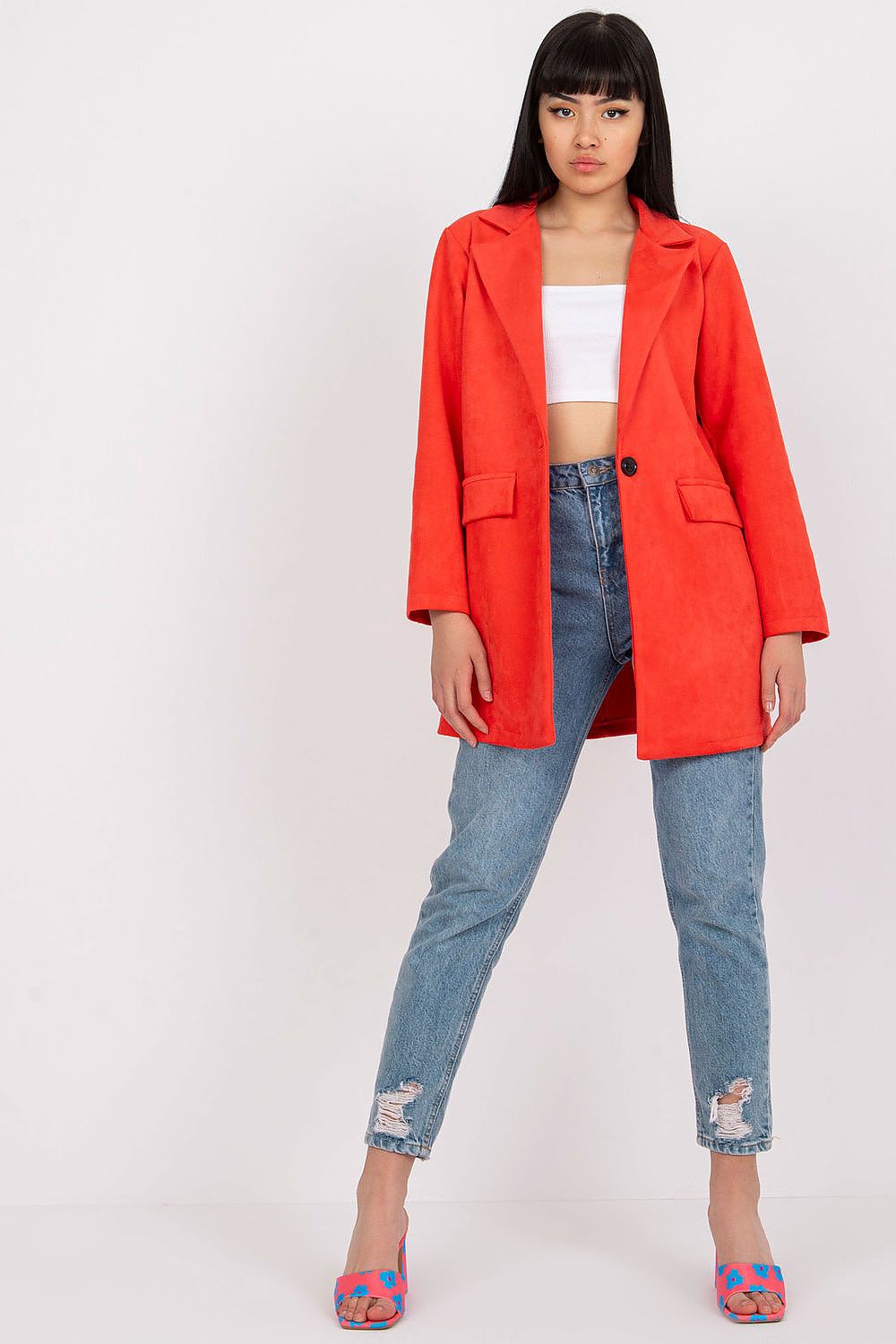 Chic model in a striking red imitation suede jacket and cropped top, standing confidently in distressed jeans and colourful heels, embodying modern elegance for a fashionable outfit.