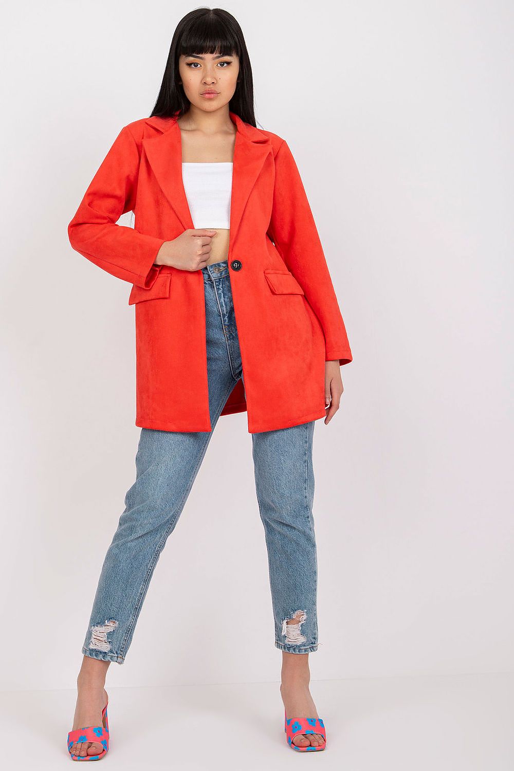Elegant model showcasing a red imitation suede jacket, styled with ripped denim and vibrant heels, epitomising contemporary fashion with a luxurious twist.