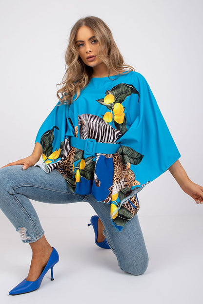 Sophisticated Italy Moda loose cut blouse in a striking blue hue adorned with bold prints, styled with light blue jeans and chic blue heels, delivering an air of modern elegance.