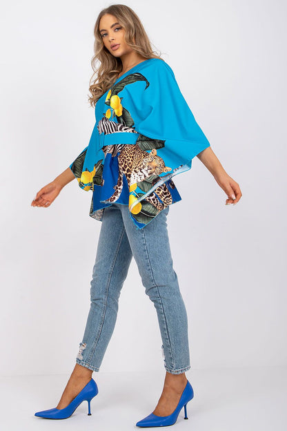 Glamorous profile shot of Italy Moda loose cut blouse in vivid blue design, enhanced with a stylish belt, teamed with light jeans and sophisticated blue pumps, exuding contemporary luxury.