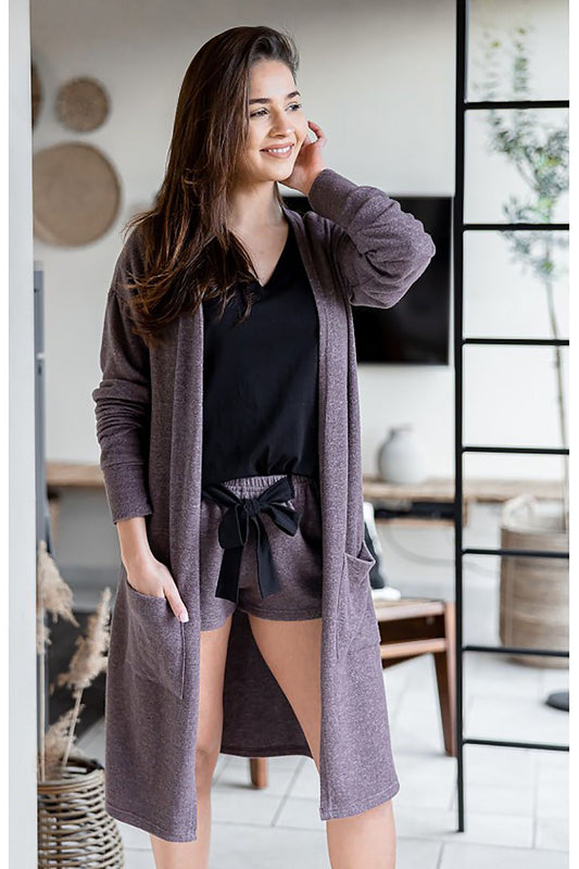 Elegant woman wearing a luxurious soft knit long cardigan by Sensis, showcasing a chic and comfortable style with side pockets, paired with stylish shorts. Ideal for a sophisticated yet casual look in a modern interior setting.