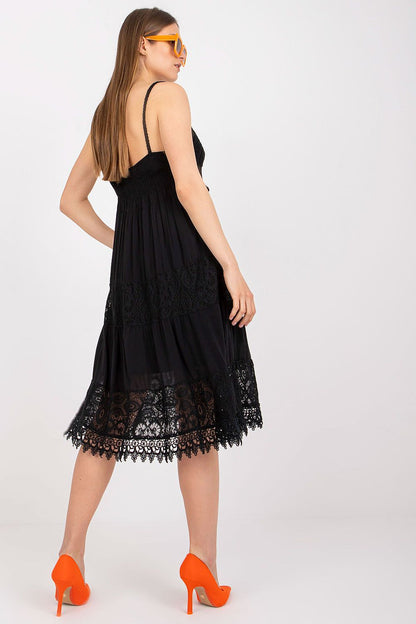 Glamorous black Och Bella Summer Flared Dress, featuring a heart neckline and exquisite lace trim, modelled with an elegant pose and striking orange footwear.