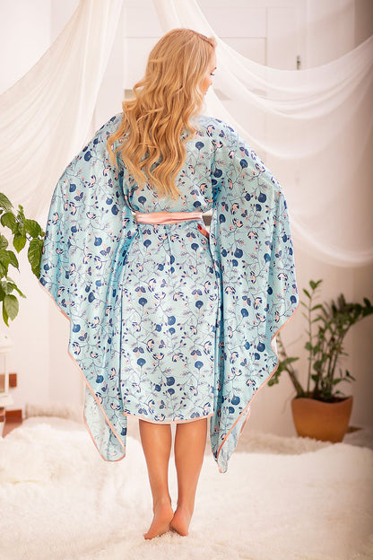 Back view of the luxurious Kalimo Satin Chemise Bathrobe, displaying the intricate floral pattern and graceful wide sleeves as the model stands in a beautifully styled indoor space, perfect for elegant relaxation.