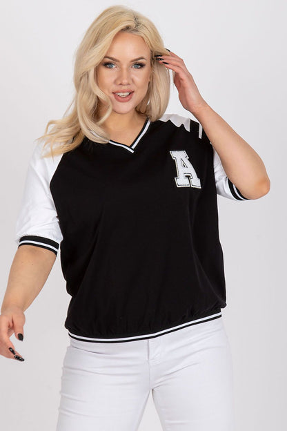 Confident model showcasing a black oversized blouse with white sleeves and an embroidered 'A' patch, combining style and comfort effortlessly.