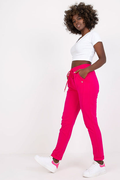 Stylish woman showcasing luxury high-waist BFG tracksuit trousers in vibrant pink, complemented by a fitted white crop top and white sneakers, exuding chic comfort.