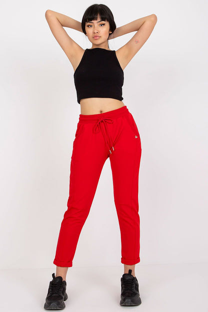 Confident woman displaying a chic ensemble featuring luxury red high-waist BFG tracksuit trousers and a fitted black crop top, accentuated by sporty black trainers, embodying stylish versatility.