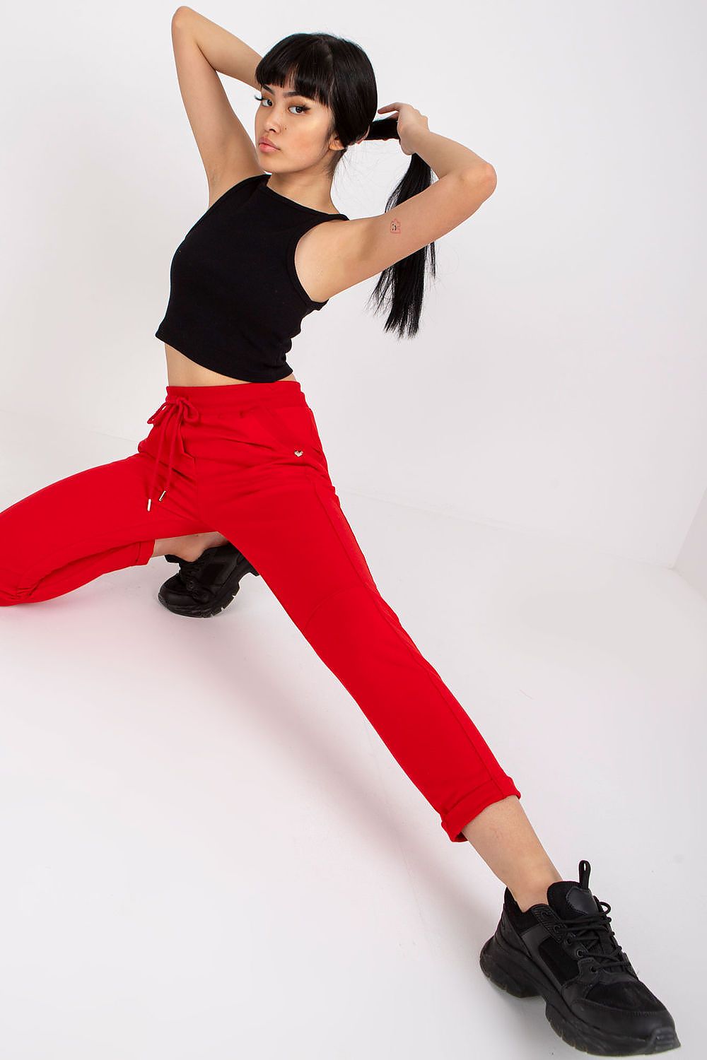 Model showcasing red luxury high-waist tracksuit trousers with slip pockets, styled with a black crop top and sporty black sneakers, in a dynamic pose.