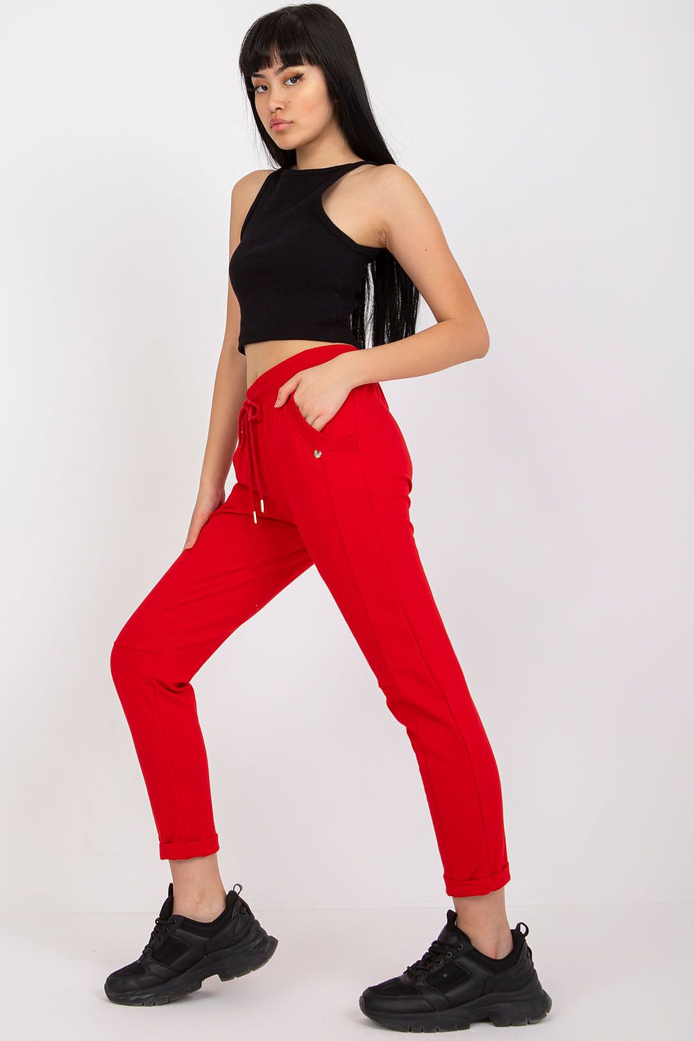 Model elegantly posing in red high-waist tracksuit trousers featuring slip pockets, paired with a sleek black crop top and trendy black sneakers.
