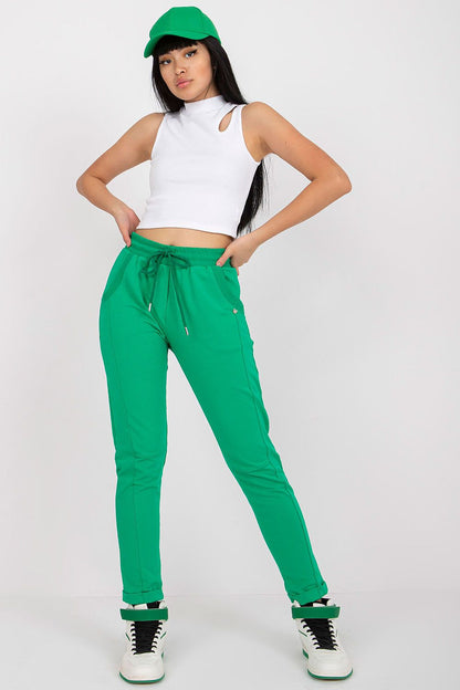 Chic model in green luxury tracksuit trousers with slip pockets, styled with a white crop top and a green cap, capturing a fashion-forward look.