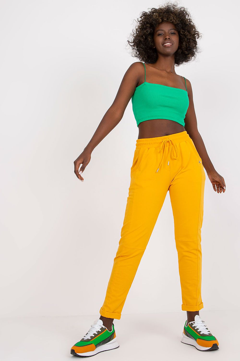 Elegant young model showcasing luxurious high-waist tracksuit trousers in vibrant yellow paired with a stylish green crop top: perfect for casual outings.