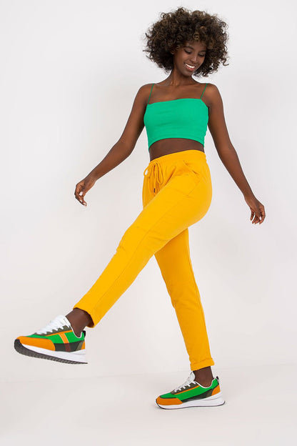 Fashionable model demonstrating playful movement in yellow tracksuit trousers and a green crop top, ideal for luxury casual wear.