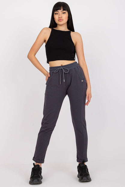 Trendy young woman in grey high-waist trousers and a black cropped tank top, showcasing a fusion of elegance and athletic chic in her stance.